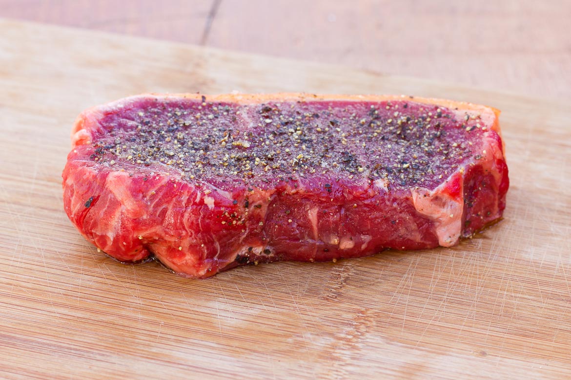 A thick cut of New York Strip Steak seasoned with salt and pepper